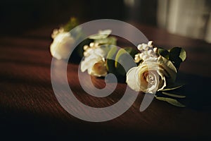 The bride holding in hand close-up the groom`s buttonhole flowers with white roses, and green and greenery