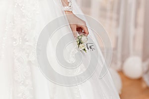 The bride holding in hand the groom`s buttonhole flowers with white roses, and green and greenery. Bride`s Preparations