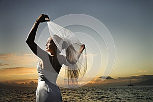 Bride holding veil on beach