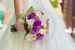 Bride holding violet wedding carnation bouquet against gown