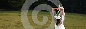 Bride holding white bouquet over head in nature