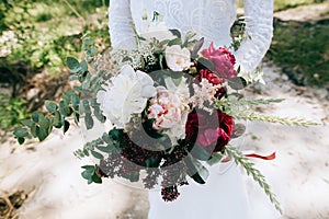 Bride holds beautiful wedding bouquet with red peonies and eucalyptus leaves in rustic and boho style