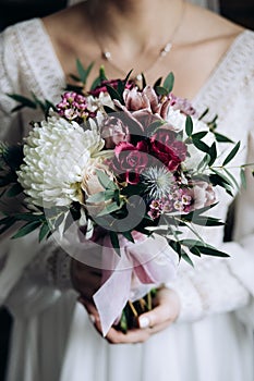 The bride holds a beautiful wedding bouquet of white chrysanthemums and purple roses