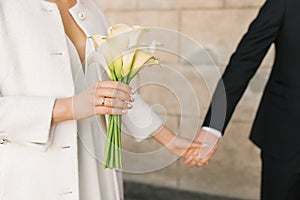 The bride holds the groom`s hand. Bouquet of white calla lilies in the hand of a woman in a white coat