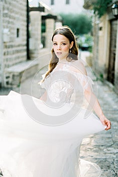 Bride holds the hem of a flowing dress on a cobbled street