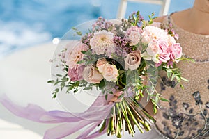 The bride holds a pink and lilac wedding bouquet in her arms against the background of the sea