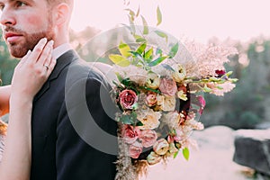 A bride holds rustic wedding bouquet consisting of different flowers. Bride gently touches the face of her groom