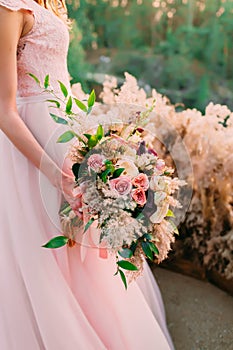 A bride holds rustic wedding bouquet consisting of different flowers. Decoration Artwork