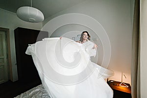 The bride holds a wedding dress in her hands and spins, turn with her on the bed. Style vintage elegant dress with lace. Wedding