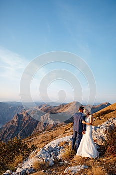 The bride hug the groom and hold his hand on the top of Mount Lovcen overlooking the Bay of Kotor, smile and hug