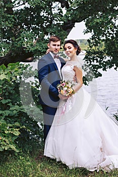 Bride hugging groom on the river bank under a tree