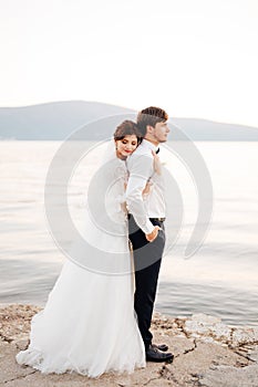 The bride hugs the groom, resting her head on his back on the pier near water