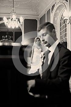 Bride kisses groom's cheek while he plays on the piano