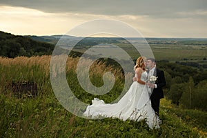 Bride kisses groom's face tenderly while they stand on a green h