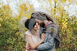 Bride in a knitted hat with a pom pom, hat covering her eyes. Groom in a colorful scarf. Wedding ceremony outdoors.