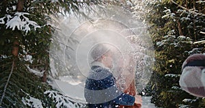 bride laughing hugging kiss groom hat denim jacket under falling snow in forest Christmas tree