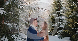 bride laughing hugging kiss groom hat denim jacket under falling snow in forest Christmas tree