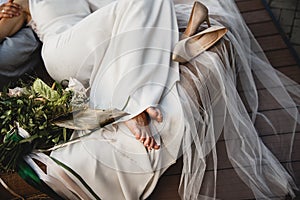 A bride is laying on the couch barefoot, her shoes are laying beside her. She is wearing a white wedding dress