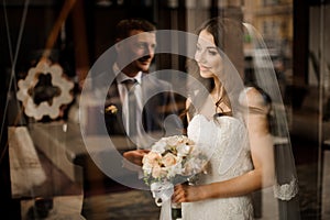 Bride looks out the window at the reflection of groom