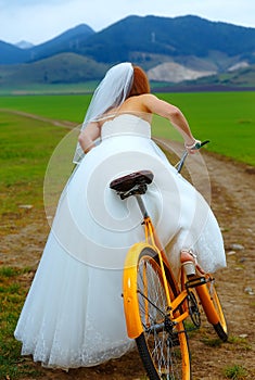 Bride on orange bike in beautiful wedding dress with lace in landscape. wedding concept.