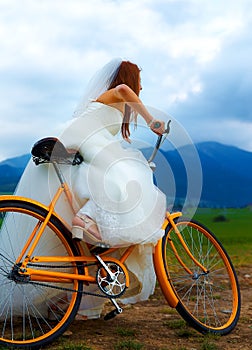 Bride on orange bike in beautiful wedding dress with lace in landscape. wedding concept.