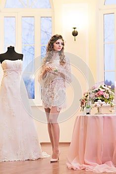 Bride in a peignoir standing next to her wedding dress