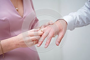 Bride in pink dress puts on wedding ring on grooms finger. Closeup shot, only hands of just married visible. Wedding moment