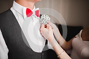 Bride pins white boutonniere with green leaves to groom`s jacket