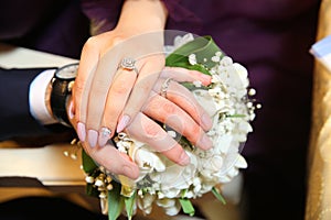 The bride put her hand on her husband`s hand with wedding rings . The newlyweds put their hands on a engagement white bouquet of