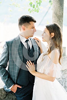 Bride put her hand on the shoulder of the groom standing in a stone gazebo