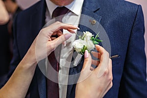 Bride puts groom on boutonniere from pink and whote rose on wedding day photo