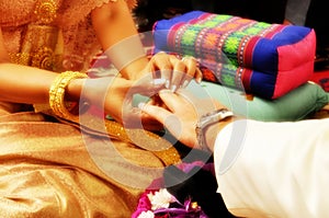 The bride puts the ring on the groom`s finger during a traditional Thai wedding