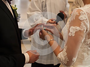 The bride puts the wedding ring on the groom`s finger during the ceremony in church under the supervision of the priest, Czech Rep