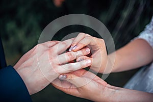 Bride putting gold wedding ring on groom`s finger during wedding ceremony, close up, blurred background