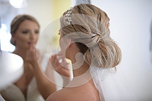 The bride putting on lipstick in living room front of mirror