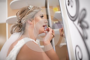 The bride putting on lipstick in living room front of mirror