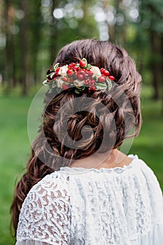 Bride with red natural flowers and greenery in her hair. Portrait of attractive young woman with beautiful hairstyle and stylish h