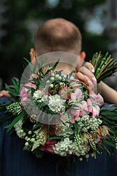 Bride`s arms around grooms neck she is holding colorful wedding bouquet close up