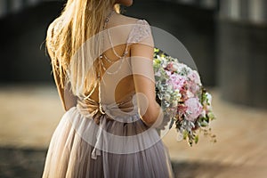 Bride`s back in a lace wedding dress. Woman holds a bouquet of pastel flowers and greenery