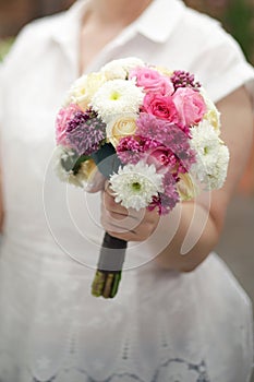 bride`s bouquet in her hands on the background of the bride`s white dress. flowers in a bouquet