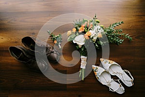 The bride`s bouquet with large white roses and the groom`s boutonniere with women`s white shoes and men`s brown shoes