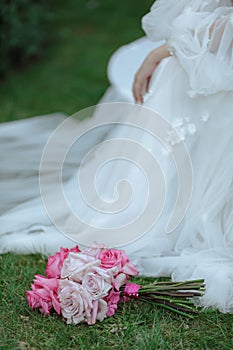 Bride's bouquet in pink tones lies on lawn against background of white wedding dress. Accessories.