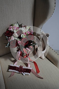 A bride`s bouquet of red and pink roses, women`s shoes, a garter of the bride