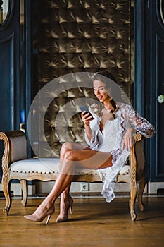 Young beautiful bride in white negligee watching a message in her smartphone