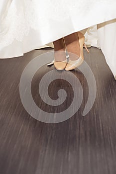 Bride`s feet in shoes playfully peek out from under the hem of a wedding dress