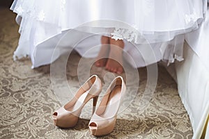 Bride`s feet in shoes under wedding dress.