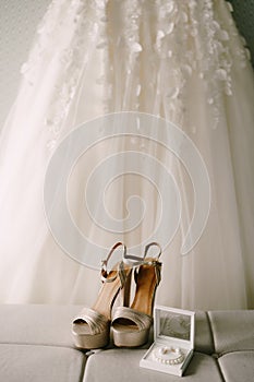 The bride`s gold wedding shoes, earrings and a pearl bracelet on the background of the wedding dress.