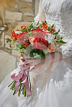 bride's hands hold a wedding bouquet of red and pink roses tied with pink ribbons. beautiful manicure  lace white
