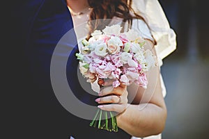 bride's hands hold a wedding bouquet of white and pink roses tied with pink ribbons. beautiful manicure  golden