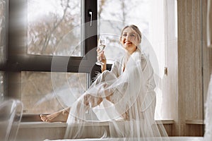 Bride s morning. Bride drinking champagne in the peignoir. young woman is sitting on a large window in a hotel room in